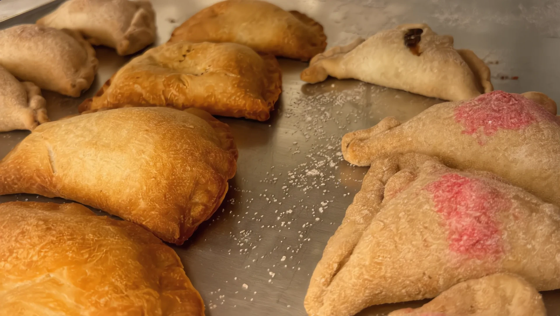Golden sugar-dusted empanadas and turnovers on a bakery tray, edges crimped by hand.