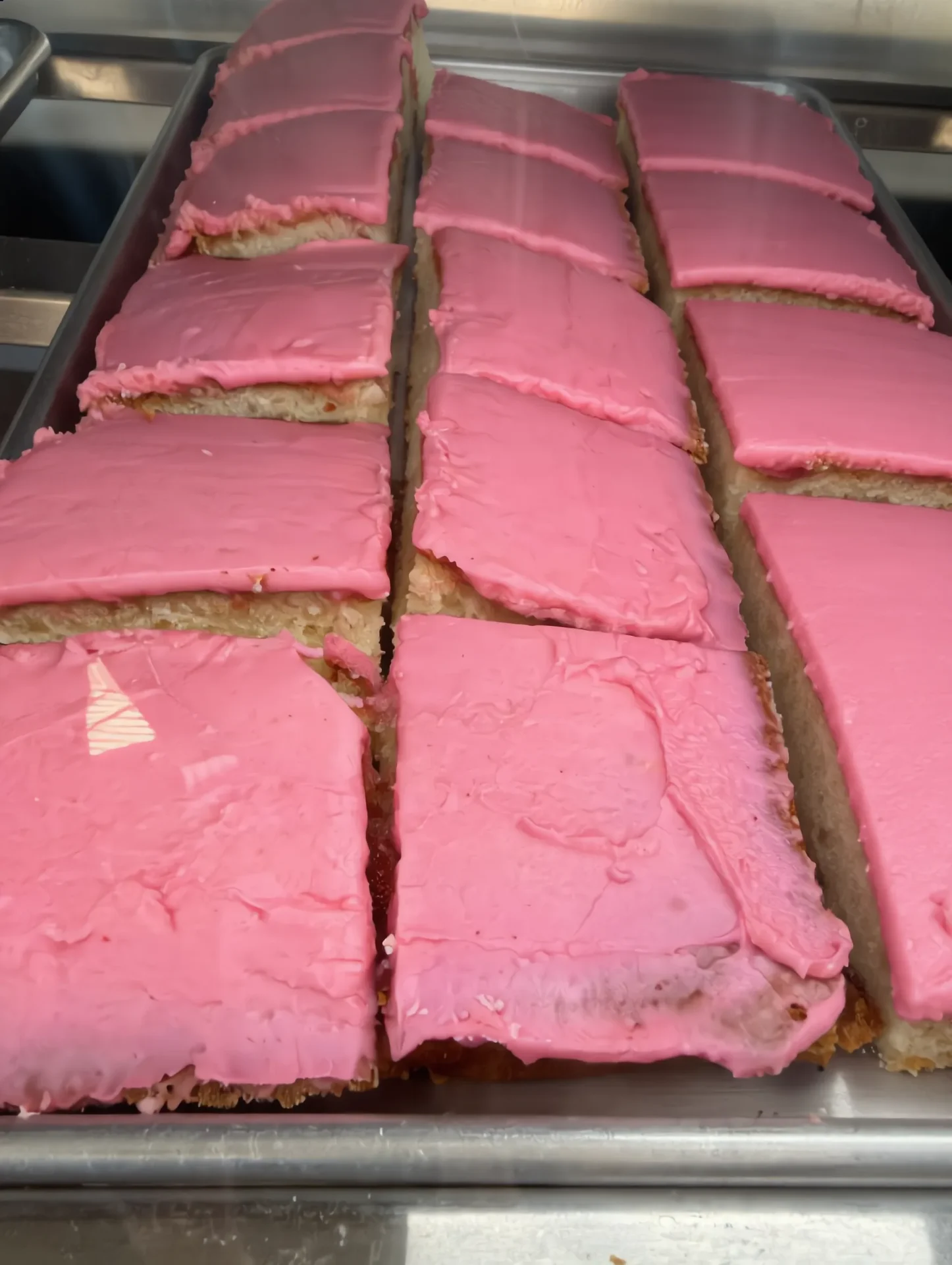 Sheet tray of pink-iced bar slices fresh from the bakery kitchen, frosting smooth and vibrant.