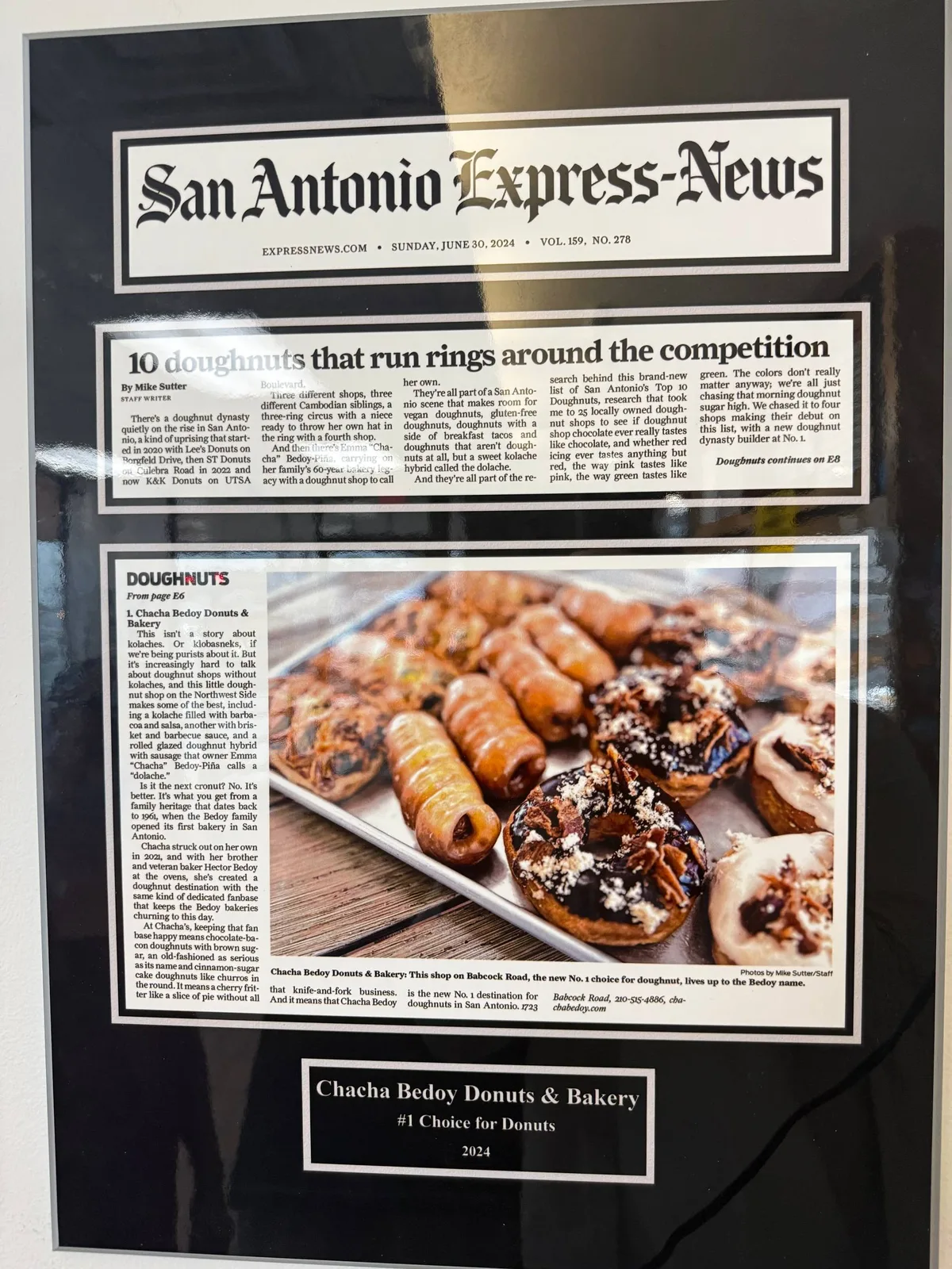 Framed San Antonio Express-News clipping from June 30, 2024 on the bakery wall, headlined '10 doughnuts that run rings around the competition,' with ChaCha Bedoy ranked #1 and a tray of doughnuts and dolaches in the photo.